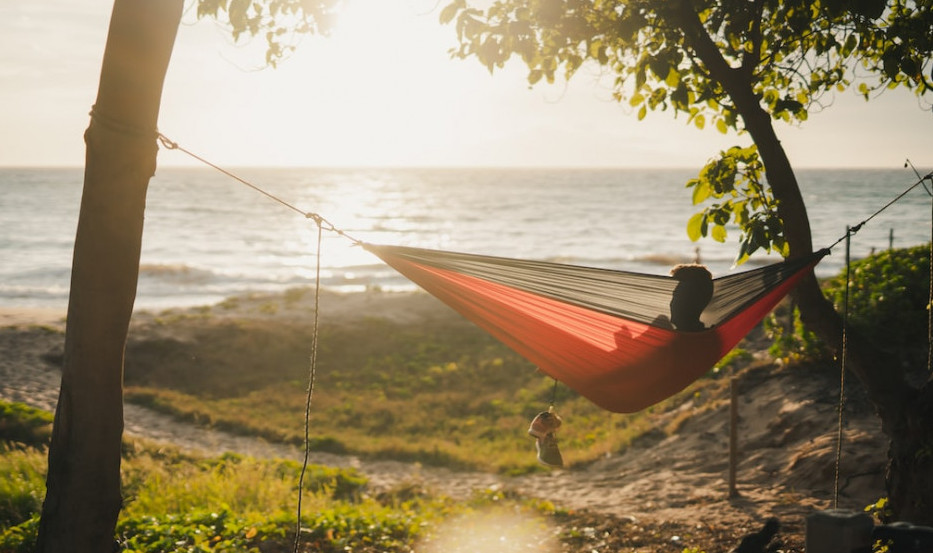 A person lying in a hammock near the ocean