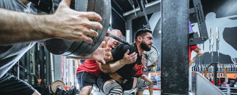 A man being spotted while squatting