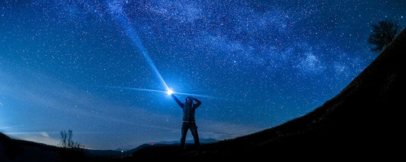 A person pointing a light into the night sky